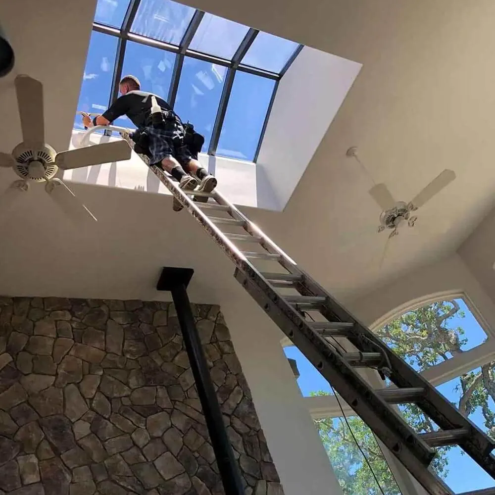Cleaning a high interior atrium window from a ladder inside a vaulted ceiling home