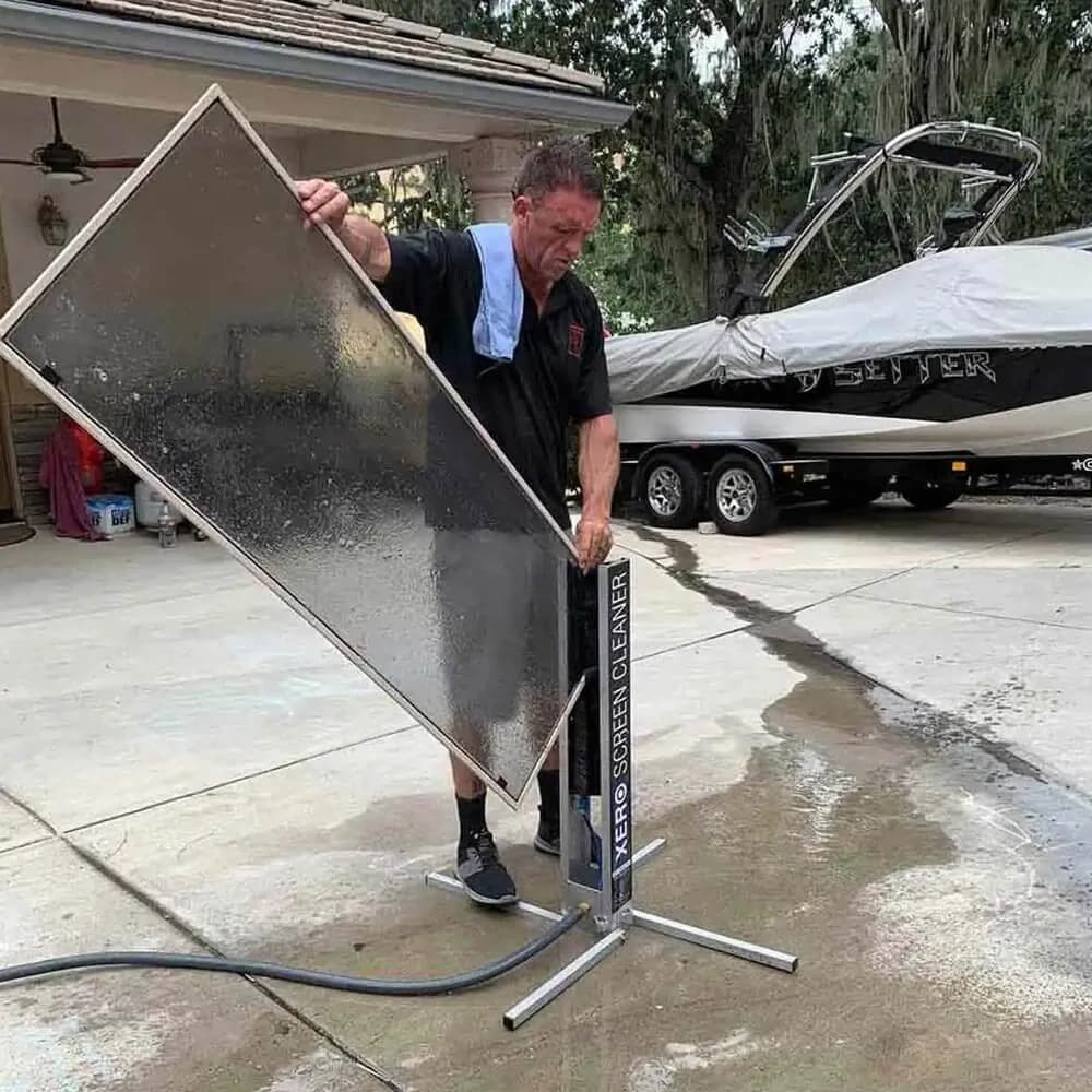 Cleaning a large removed glass panel on a stand outdoors beside a boat