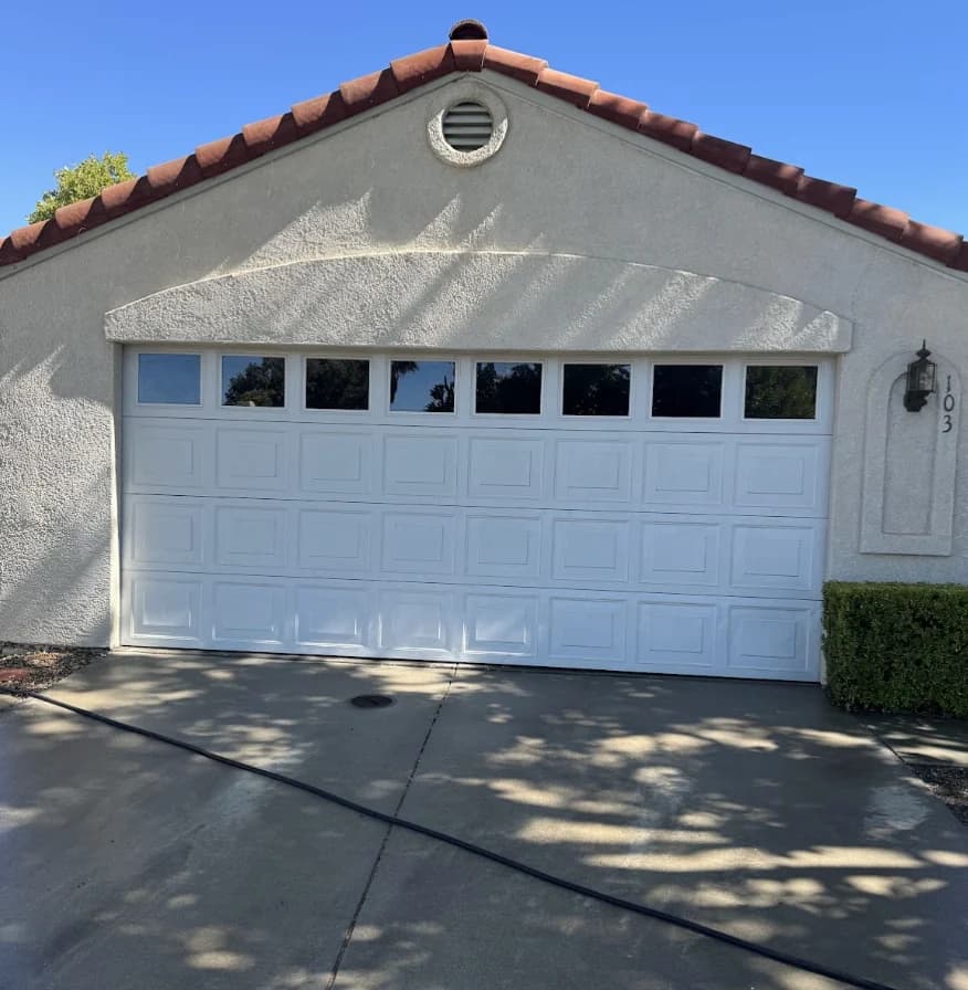 Clean white garage door and stucco frontage on a tile roofed home after soft washing